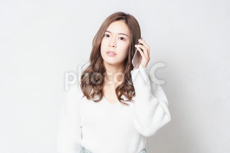 白い壁の前に立って、スマホを使う若い女性 スマホ,メール,携帯の写真素材