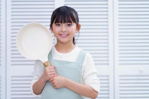 エプロン姿でフライパンを持つ子どもの笑顔 女の子,フライパン,持つの写真素材