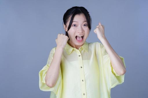 両手で大喜びを表現する黄色い服の女性の写真