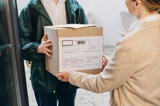 玄関で女性に配達物を渡す配達員の男性 配達,フードデリバリー,デリバリーの写真素材