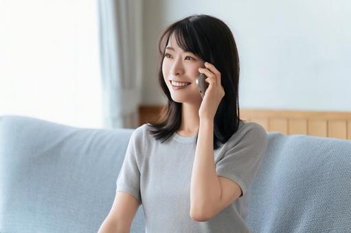 ソファに座ってスマホで話す笑顔の女性 ソファに座ってスマホで話す笑顔の女性 女性,スマホ,スマートフォンの写真素材