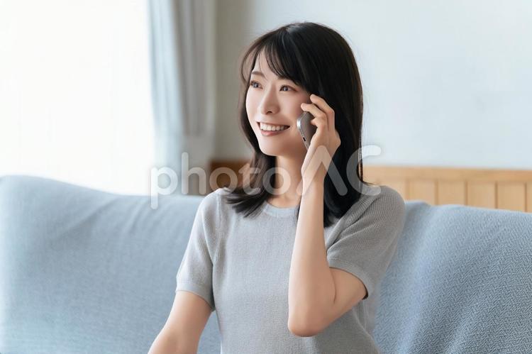 ソファに座ってスマホで話す笑顔の女性 女性,スマホ,スマートフォンの写真素材