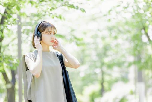 新緑の中ヘッドフォンで音楽を聴く若い女性 新緑の中ヘッドフォンで音楽を聴く若い女性 女性,外出,ヘッドフォンの写真素材