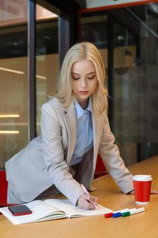 立ったままテーブルのノートに書き込んでいるビジネスウーマンの写真