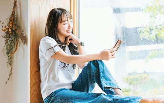 窓際でスマホを使う女性 窓際でスマホを使う女性 女性,スマホ,スマートフォンの写真素材