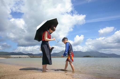 <素材>海で子供に日傘で休むよう促す母 <素材>海で子供に日傘で休むよう促す母 家族,子供,女性の写真素材