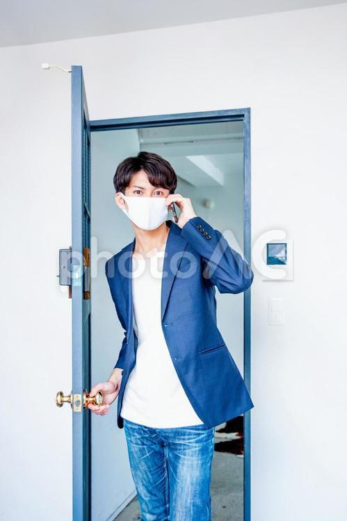 マスクをしてドアから電話して入ってくる男性 マスク,スマホ,コロナ対策の写真素材