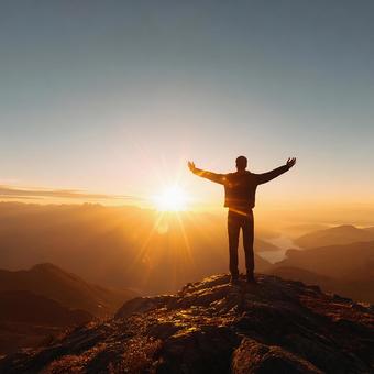山頂で夕日を浴びる男性の後ろ姿の写真