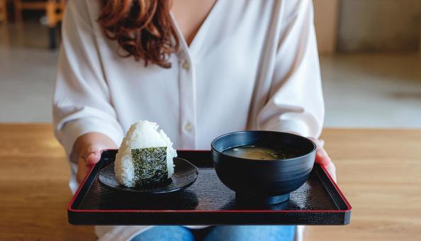 お盆に乗ったおにぎりと味噌汁を持つ女性 お盆に乗ったおにぎりと味噌汁を持つ女性の写真