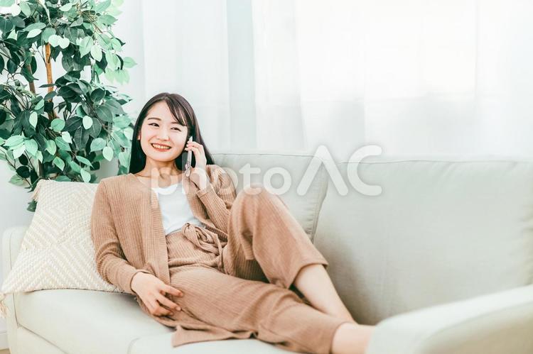 スマホで電話する日本人女性（家・ソファ） 電話,女性,ソファの写真素材