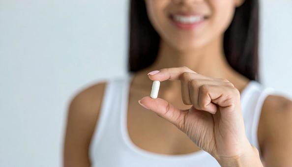 薬一錠を親指と人差し指で持つ女性 薬一錠を親指と人差し指で持つ女性の写真