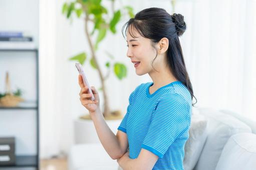 部屋でスマホを操作する女性 部屋でスマホを操作する女性 スマホ,笑顔,部屋の写真素材