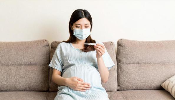 ソファによりかかり体調不良で熱を測る妊婦の写真