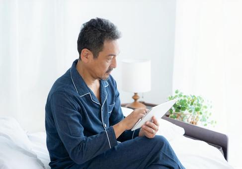 寝室でタブレットを見るミドルの男性 男性,タブレット,ミドルの写真素材