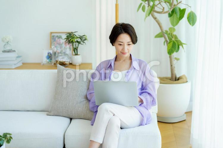 部屋でノートパソコンを使うミドル女性 女性,笑顔,テーブルの写真素材