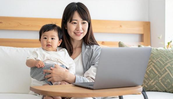 赤ちゃんを抱えてパソコンを操作する女性の写真