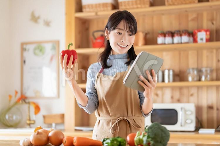 タブレットを見ながら料理をする笑顔の女性 女性,キッチン,料理の写真素材