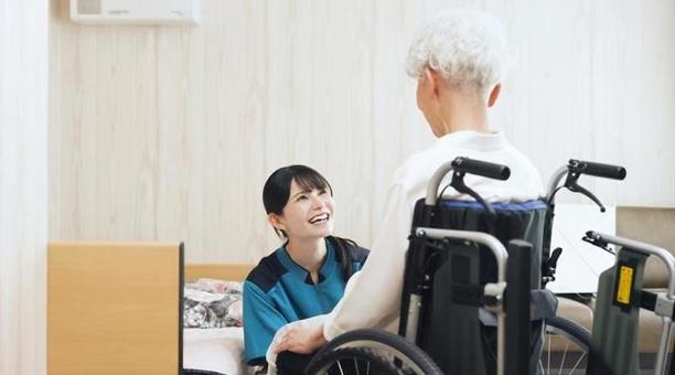 高齢者の移乗介助をするアジア人介護士 高齢者の移乗介助をするアジア人介護士の写真