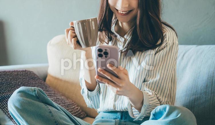 ソファでスマホを使う笑顔の女性 女性,スマホ,スマートフォンの写真素材