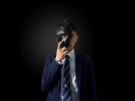 黒背景で仮面を顔に当てるスーツの男性 犯罪,不穏,不正の写真素材