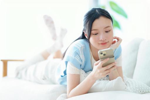 ソファで寝転びスマホを見る頬杖の女性 女性,スマートフォン,持つの写真素材