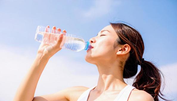 水分補給をするタンクトップの女性 水分補給をするタンクトップの女性の写真