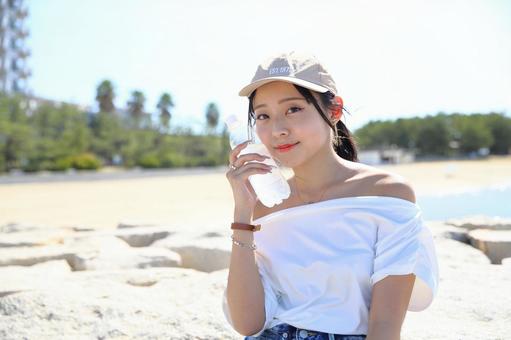 砂浜でペットボトルを頬にあてる女性 女性,ペットボトル,海の写真素材
