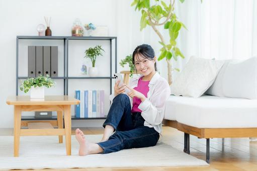 部屋でスマホを操作する若い女性 スマホ,笑顔,若い女性の写真素材