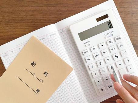 Pay envelope on desk and woman's hand calculating with calculator, JPG