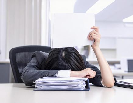 書類を持ちデスクに突っ伏する女性 書類を持ちデスクに突っ伏する女性の写真