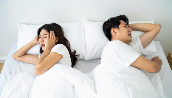 ベッドで夫のいびきで睡眠不足の妻 ベッドで夫のいびきで睡眠不足の妻の写真