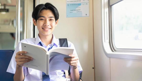 車内で読書する男子学生 車内で読書する男子学生の写真