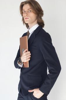 ノートパソコンを抱えているポケットに手を入れているカメラ目線のスーツの男性 男性,外国人,欧米人の写真素材