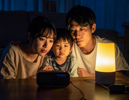 災害で停電の夜にラジオで情報収集する家族の写真
