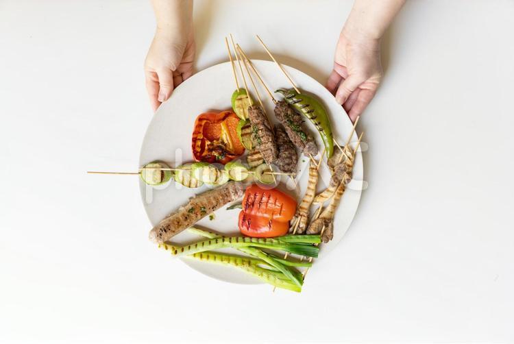 グリル野菜の入った皿を出す人の手元 手元,人物,串焼きの写真素材