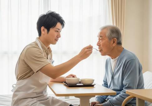 男性介護士が高齢男性に食事介助する場面の写真