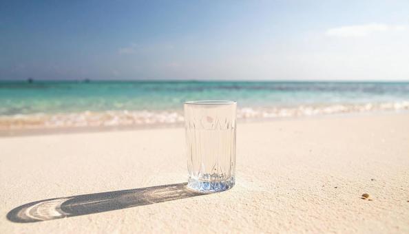 白いビーチの砂の上のグラスと水の写真