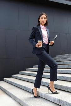 コーヒーとタブレットを持ってオフィスビルの外の階段を登るアジア人女性 ビジネスウーマン,ビジネス,女性の写真素材