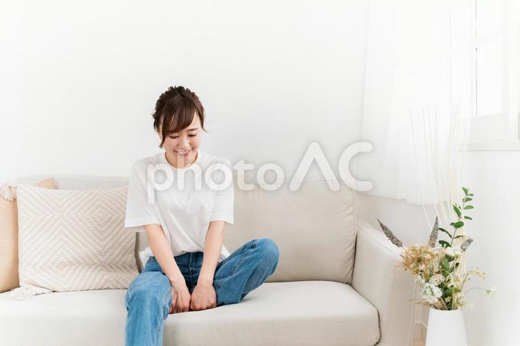 ソファに座る笑顔の日本人女性（うつむく） 女性,笑顔,ソファの写真素材