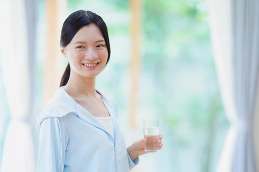 水のコップを持ち横を見て笑う女性の写真