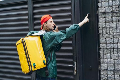 スマートフォンで話しながらインターホンを押すフードデリバリーの男性 配達,デリバリー,配送の写真素材