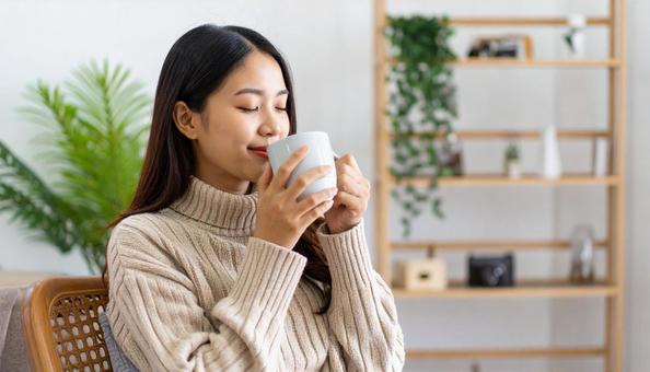 部屋でホットコーヒーを飲む女性 部屋でホットコーヒーを飲む女性の写真