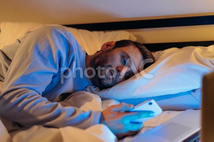 寝ながら携帯を見ている男性 男性,ヒゲ,パソコンの写真素材