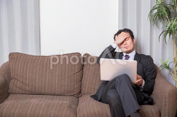 ソファでPCを開く男性 頭痛,発熱,疲れ目の写真素材