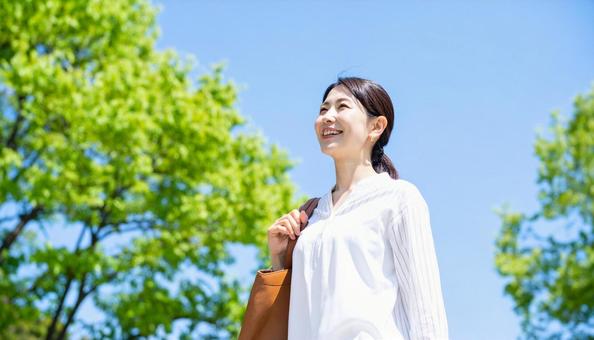 青空の自然の中を散歩する笑顔の日本人女性の写真