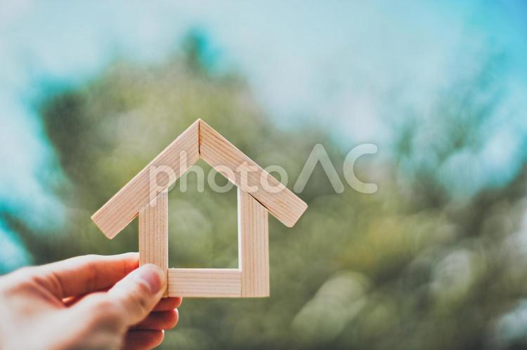木製の家を持つ人の手元と緑ぼかし背景 住宅模型,木,木製の写真素材