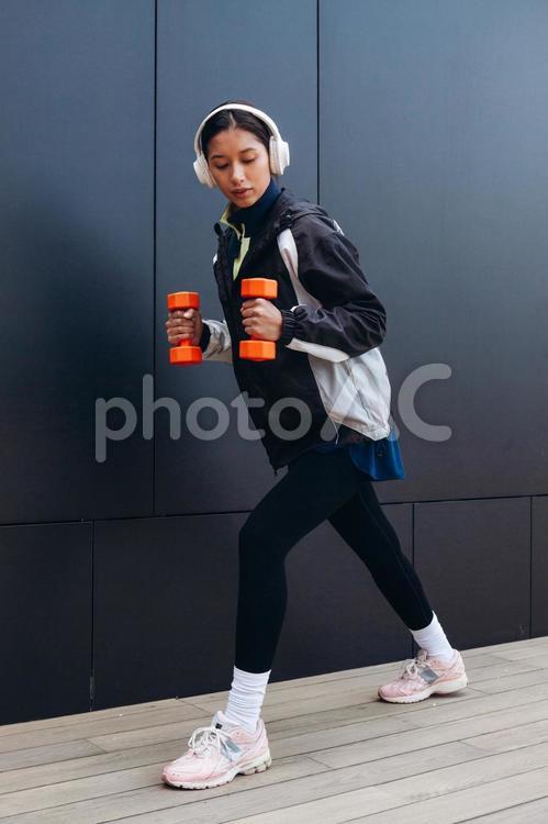 ダンベルを少し持ち上げて足を伸ばす女性 女性,ヘッドフォン,人物の写真素材