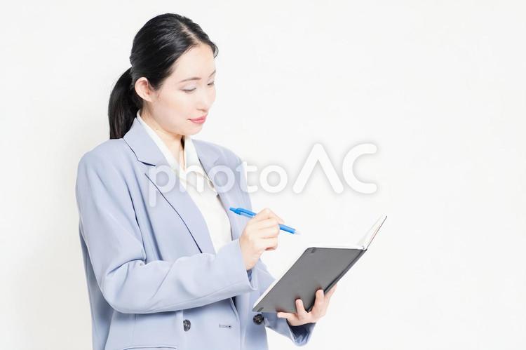 白バックの前に立って、ノートにメモを書く女性 ノート,メモ,書くの写真素材
