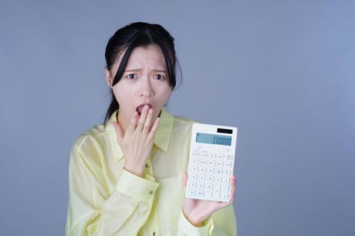 電卓を見せて驚く黄色い服を着た女性の写真