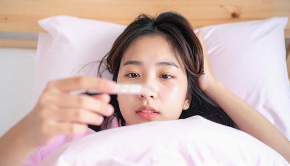 発熱して寝込んで体温計を見る女の子 発熱して寝込んで体温計を見る女の子の写真